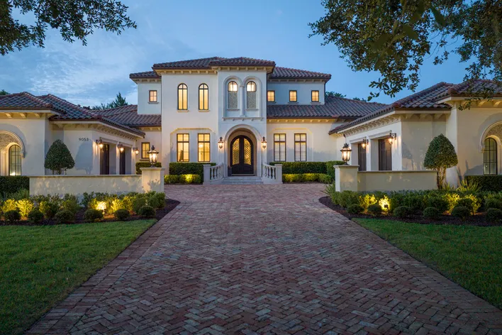 A beautiful mediterranean style home with a stone driveway at dusk.